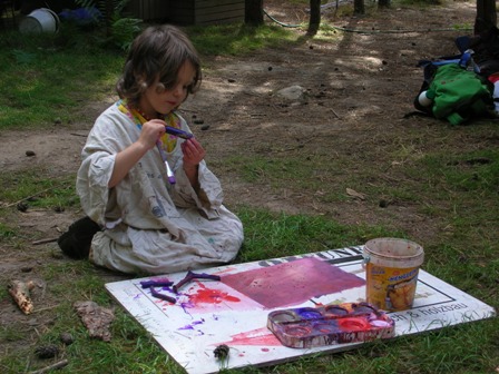 Ein Mädchen sitzt auf dem Waldboden mit einer weißen Platte mit Malutensilien
